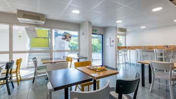 Un espace repas moderne avec des tables et des chaises, une fenêtre offrant une vue agréable et un appareil de climatisation installé au plafond.