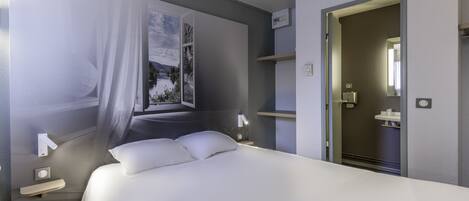 A modern hotel room with a large bed, a window with a view of a landscape, a bedside table with a lamp, and a door leading to a bathroom.