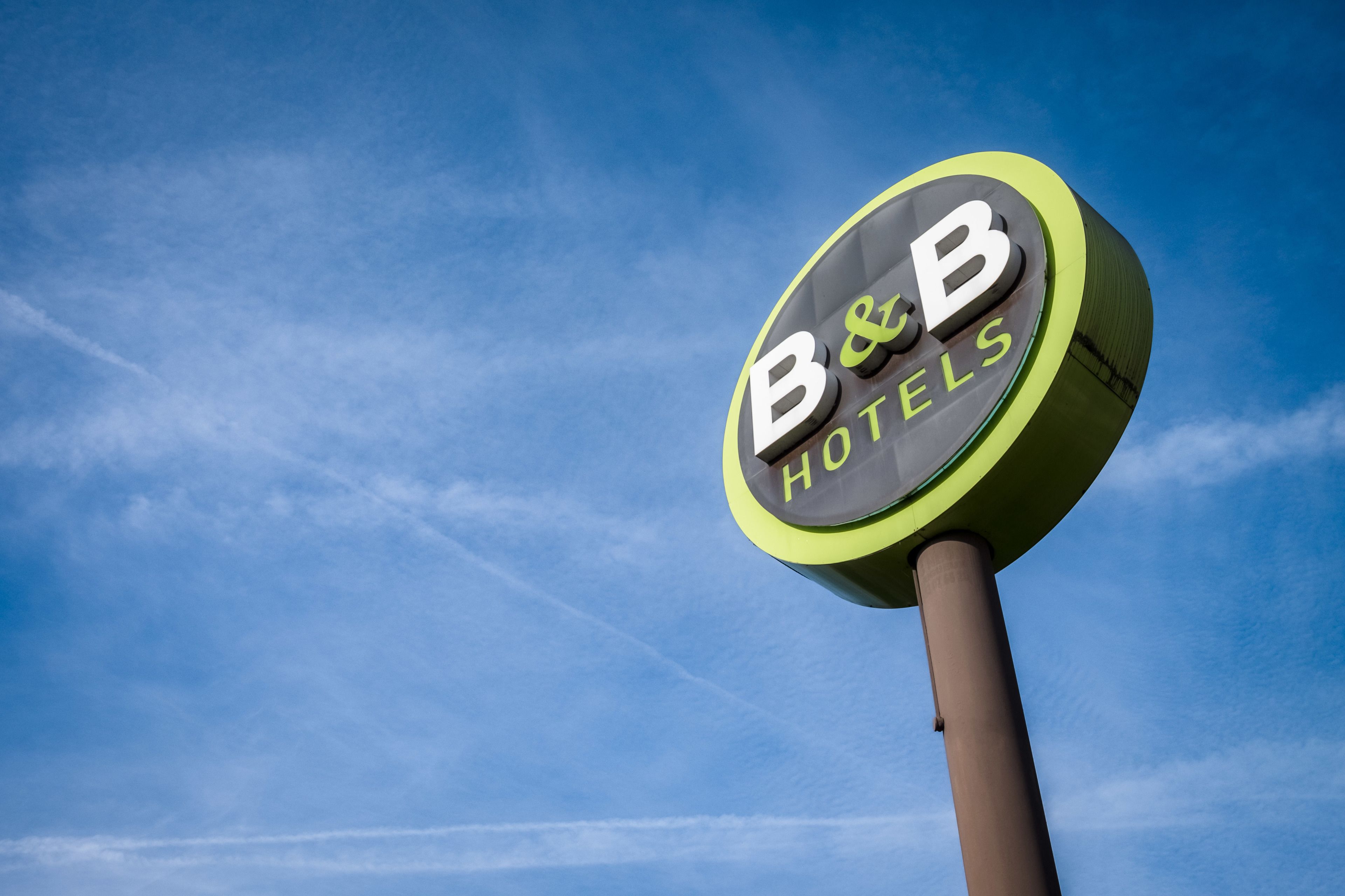 Un panneau circulaire sur lequel on peut lire « B&B HOTELS » sur un fond de ciel bleu.