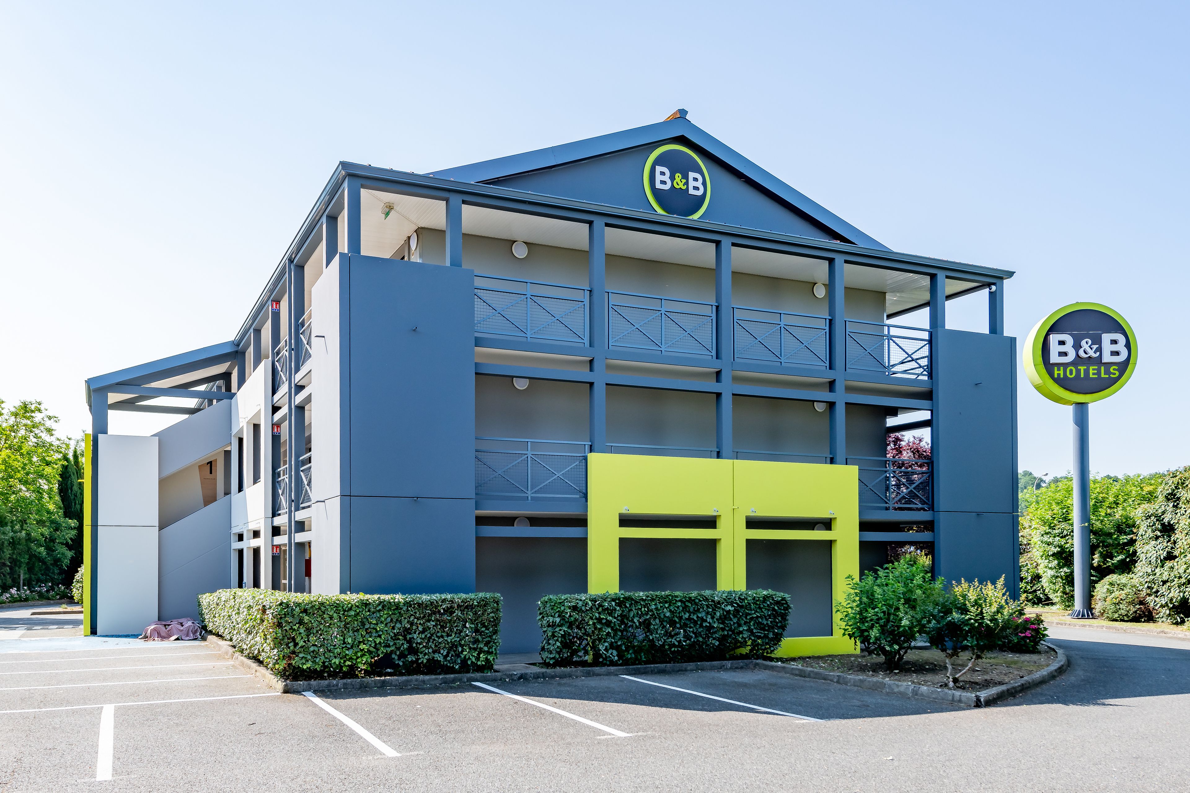 A B&B hotel with a modern design, featuring a two-story structure with balconies and a parking area in front.