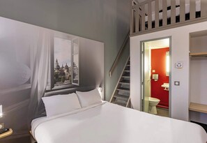 A hotel room with a bed, a nightstand, a window with sheer curtains, a staircase leading to an upper level, and a red-walled bathroom. - B&B HOTEL Périgueux Boulazac (Boulazac-Isle-Manoire)