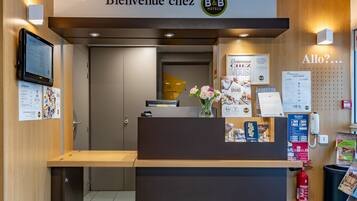 A reception desk with a digital screen, a sign reading "Bienvenue chez B&B Hotels," and various informational posters.