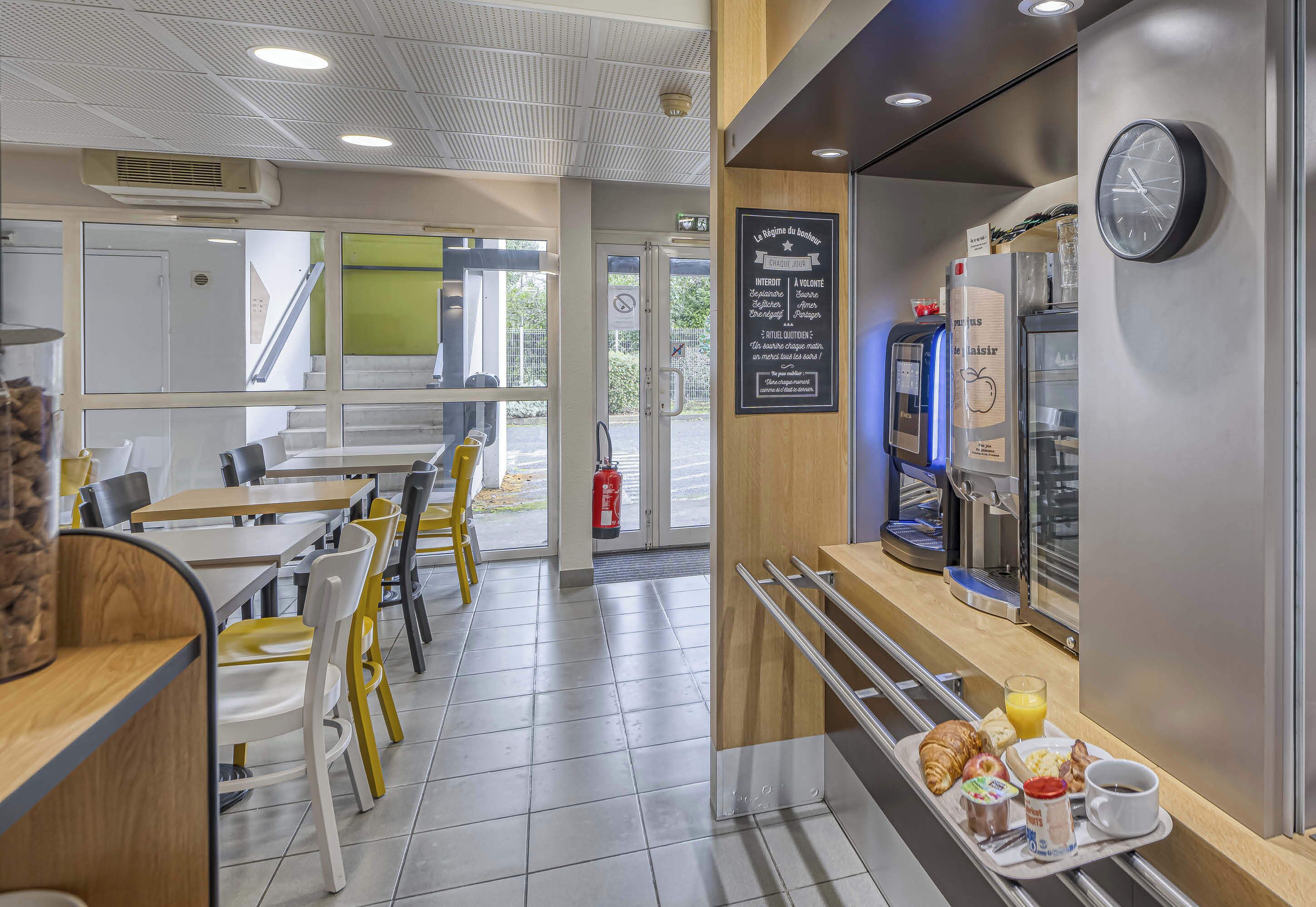 Un café moderne doté d’un bar où l’on sert le petit-déjeuner, d’un espace salon et d’une machine à café.
