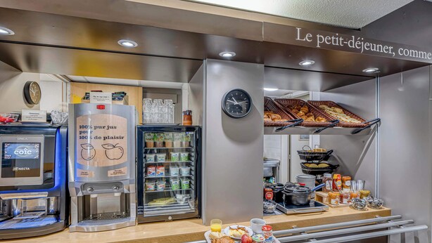 A breakfast bar with coffee machines, a refrigerator, and a clock. - B&B HOTEL Périgueux Boulazac (Boulazac-Isle-Manoire)