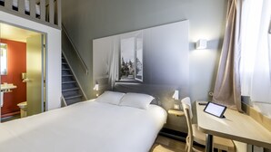 A hotel room with a bed, a desk, a chair, a nightstand, a lamp, a tablet, a window with a view, a staircase, and a door leading to another room. - B&B HOTEL Périgueux Boulazac (Boulazac-Isle-Manoire)