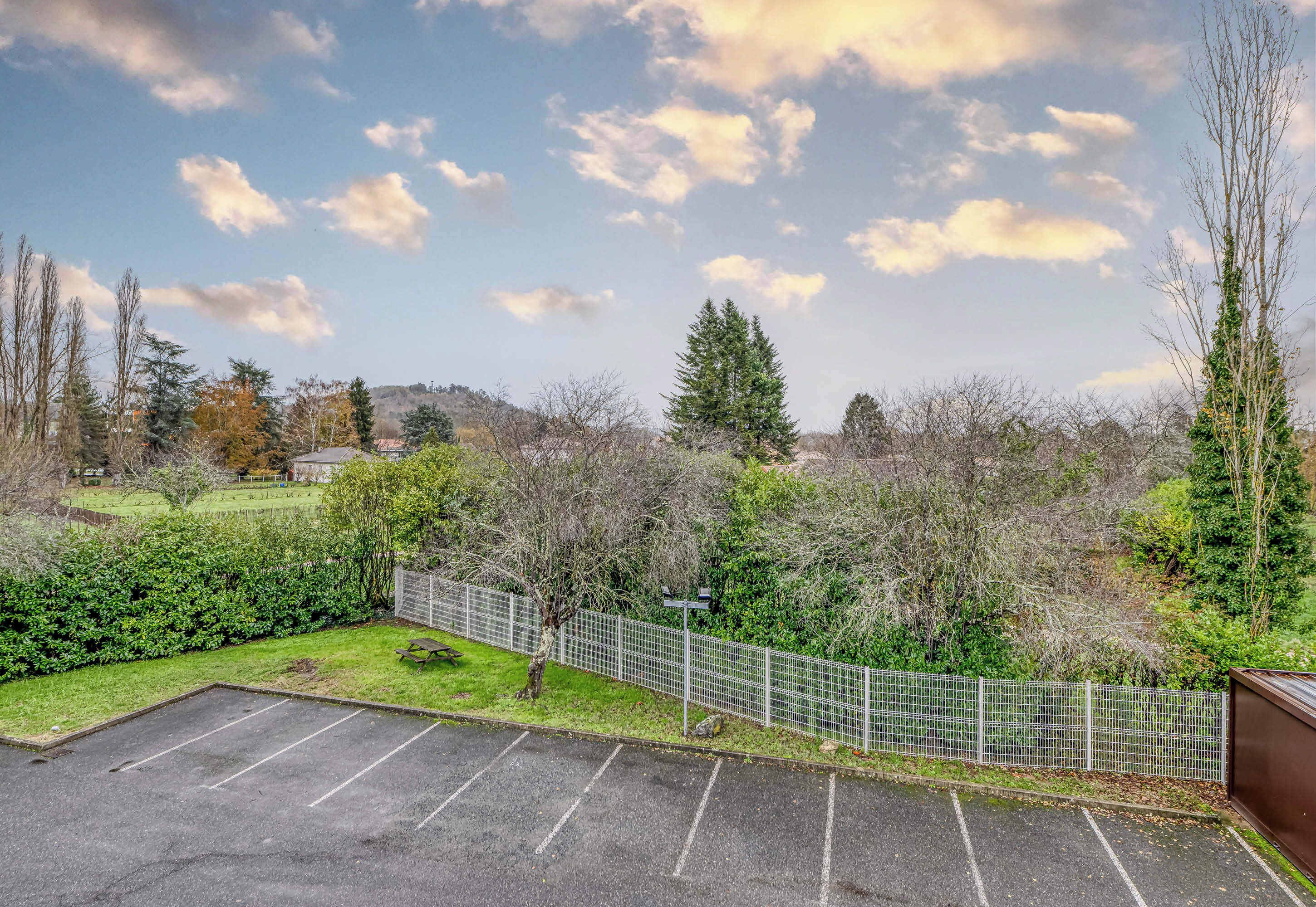 A parking lot with a fenced area, trees, and a clear sky.