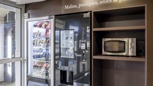 A vending machine with a selection of snacks and a microwave on a shelf. - B&B HOTEL Périgueux Boulazac (Boulazac-Isle-Manoire)