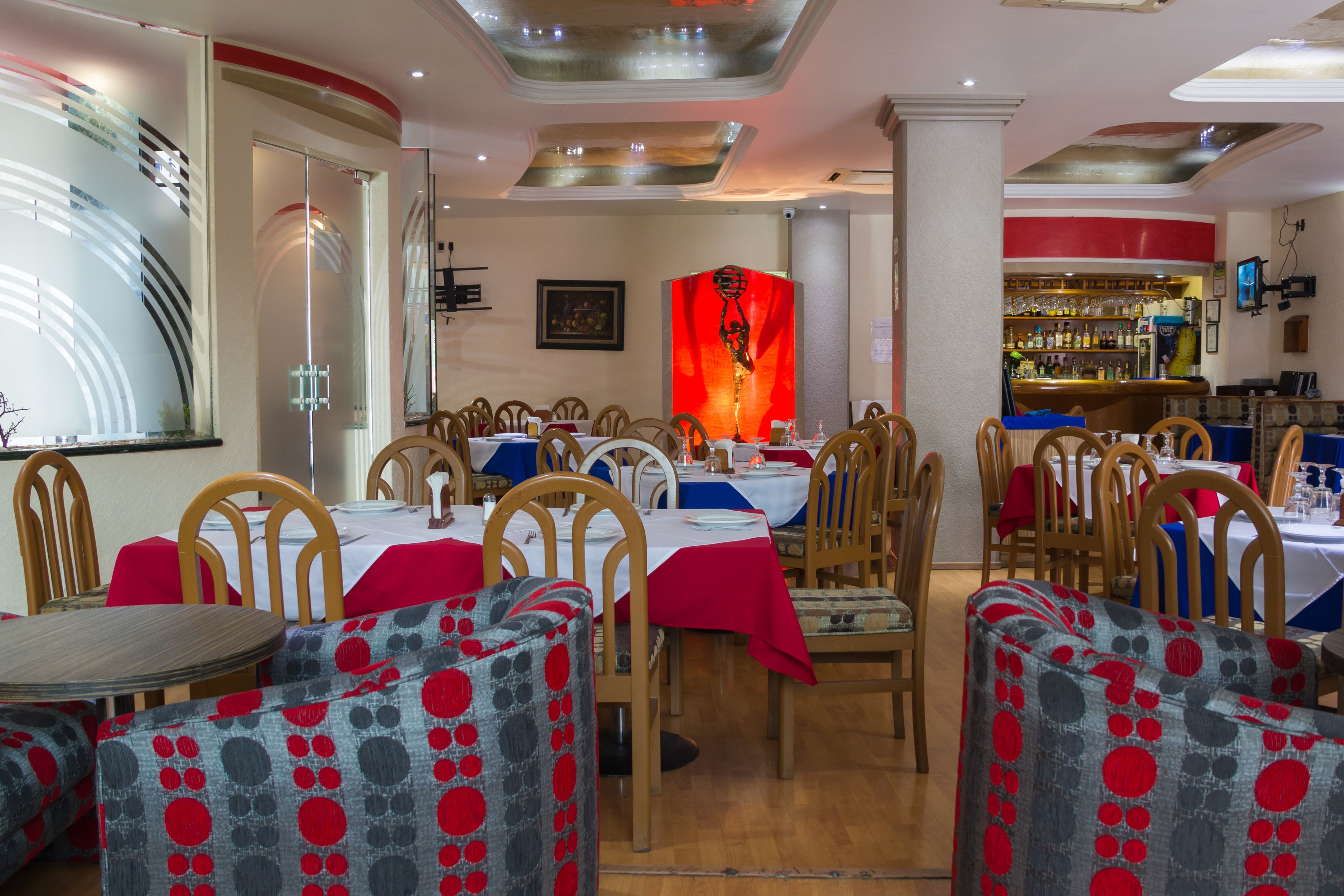 Un restaurante con mesas y sillas redondas, una zona de bar y una obra de arte roja de gran tamaño en la pared.