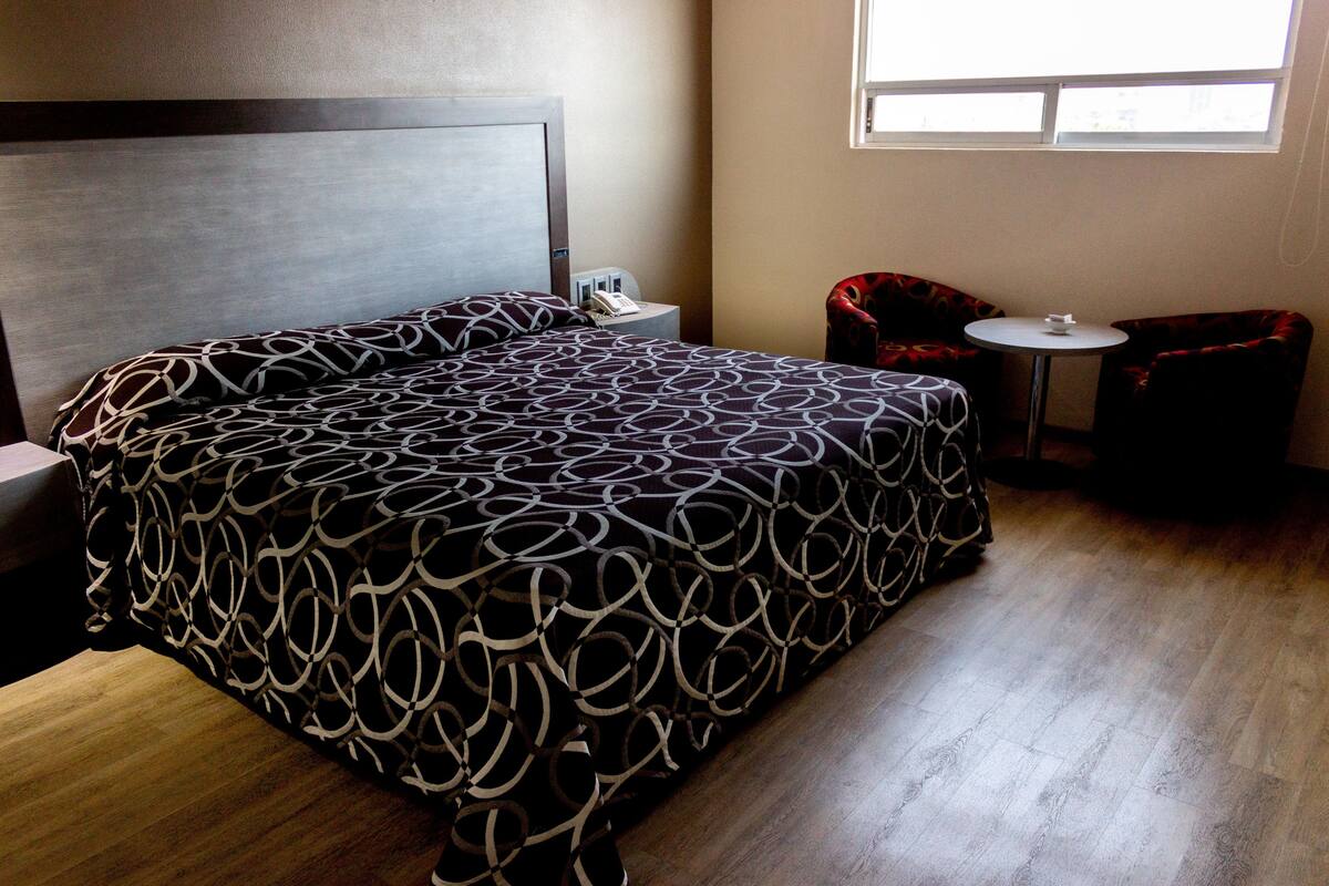 A neatly arranged hotel room with a large bed, a bedside table with a phone, a small round table, and a chair.