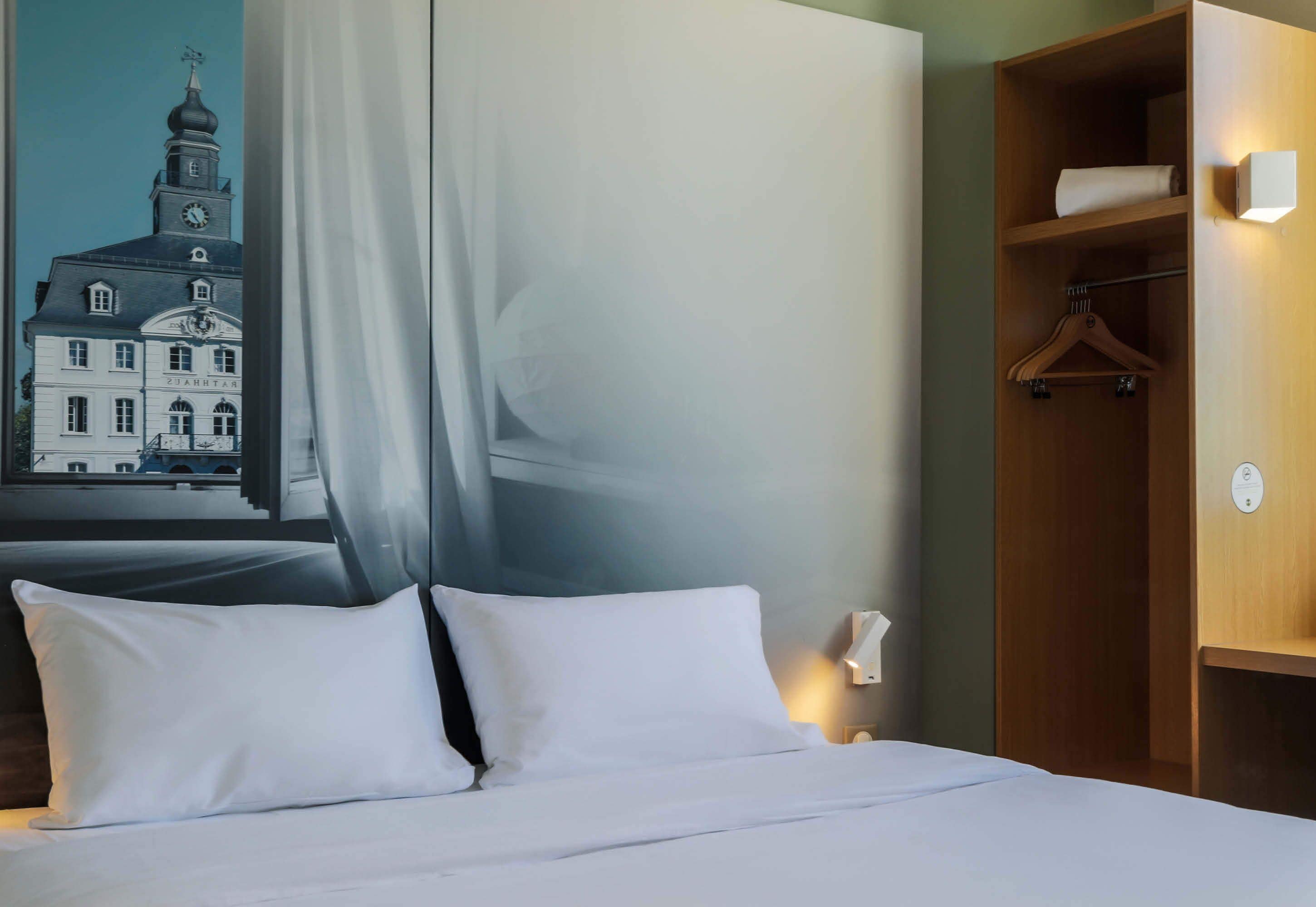 A hotel room with a bed, a wardrobe, and a painting of a building.