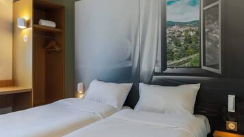 Een hotelkamer met een bed, een kledingkast, een nachtkastje en een raam met uitzicht op de stad.
