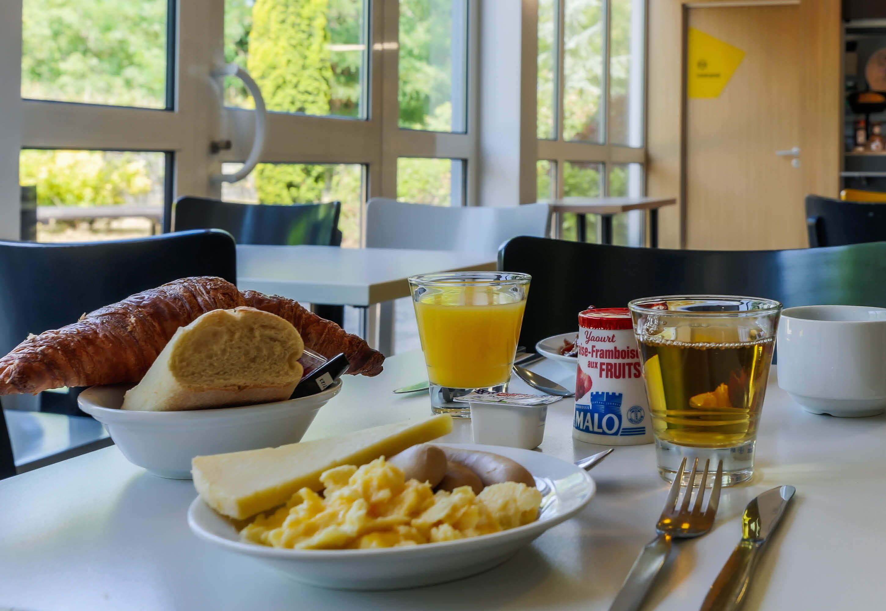 Una mesa de desayuno con cruasanes, huevos revueltos y un vaso de zumo de naranja.