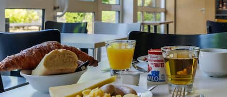 Una mesa de desayuno con cruasanes, huevos revueltos y un vaso de zumo de naranja.