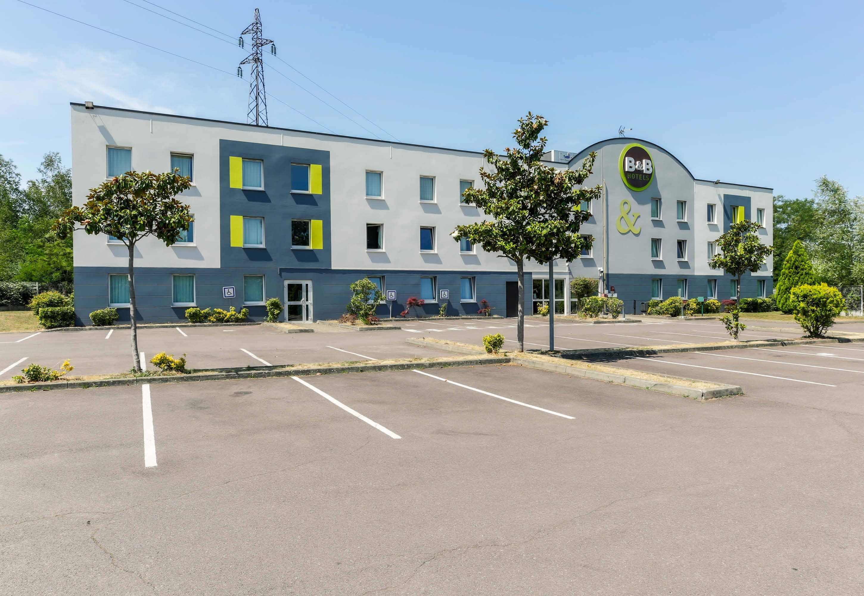 Ein modernes Hotel mit flacher Fassade, zahlreichen Fenstern und einem Parkplatz.