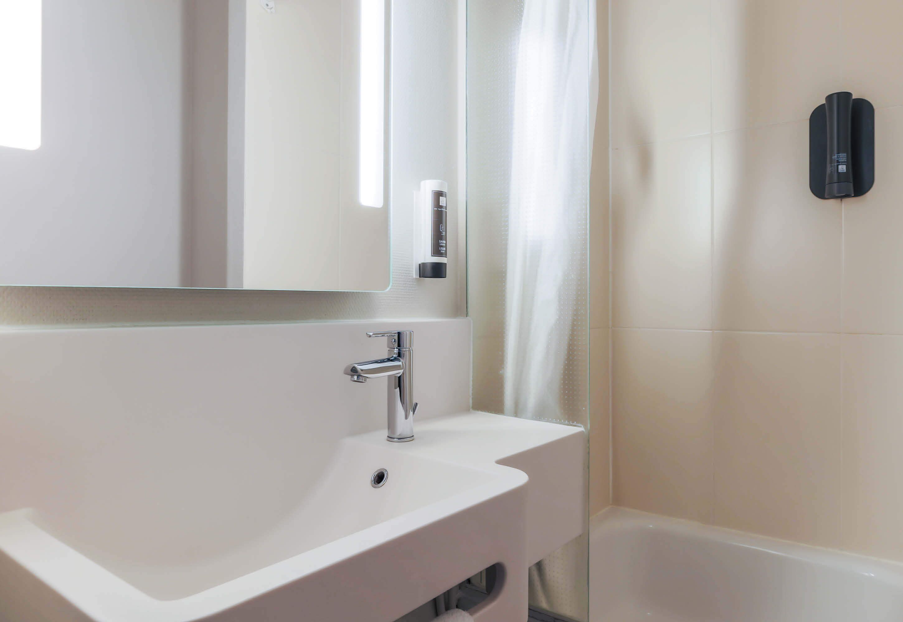 A modern bathroom with a white sink, a mirror, and a black towel dispenser.