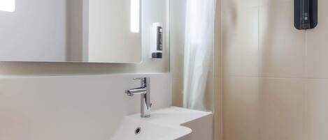 A modern bathroom with a white sink, a mirror, and a black towel dispenser.