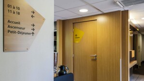 Un espace d’accueil d’hôtel avec une porte en bois, un panneau indicateur et une petite table sur laquelle se trouve une bouilloire.