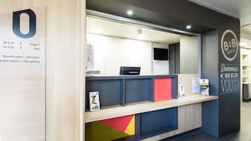 Un comptoir d’accueil avec un panneau indiquant les numéros des chambres et une enseigne d’accueil de la chaîne B&B Hotels.
