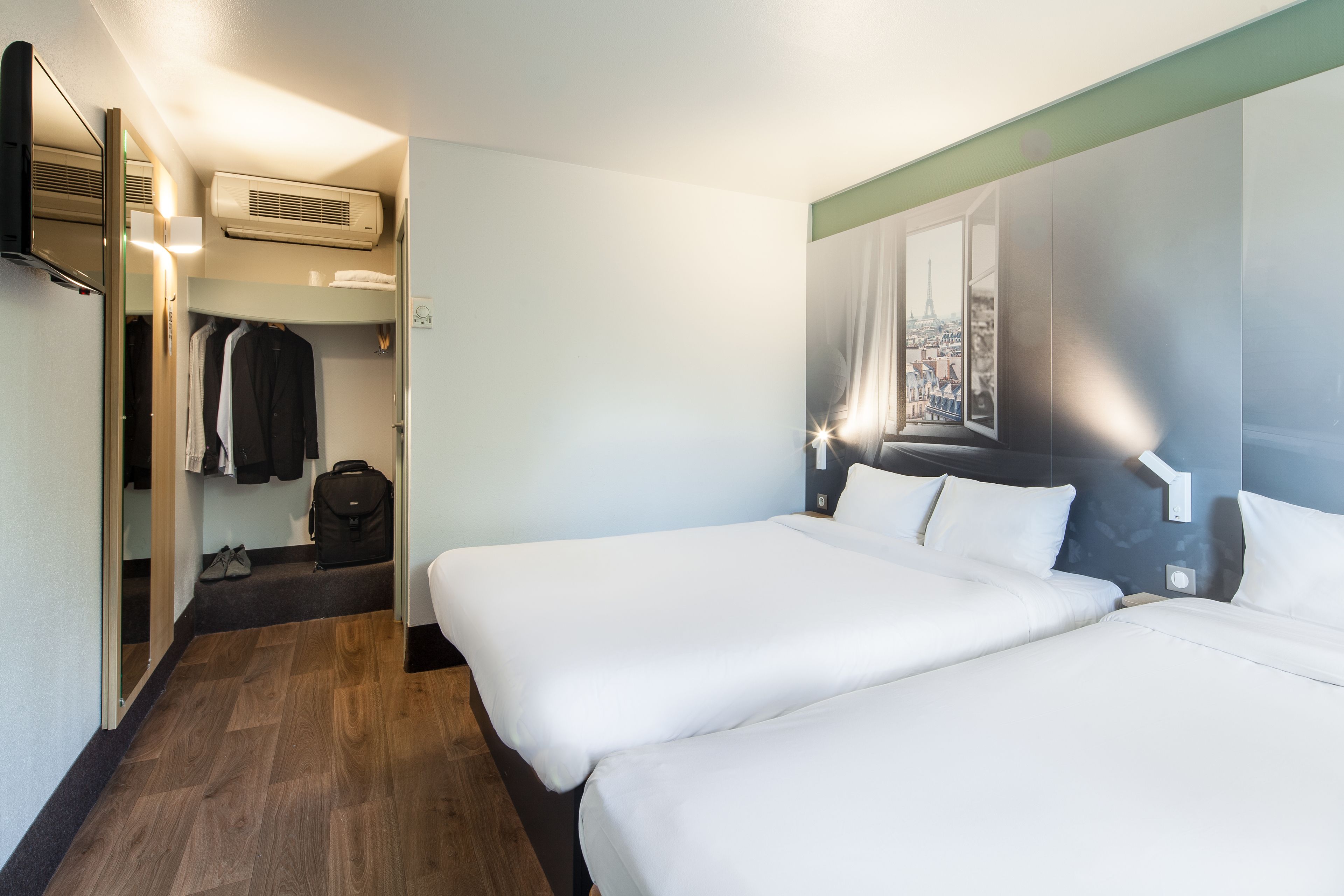 A hotel room with two beds, a wardrobe, a mirror, and a wall-mounted air conditioner.