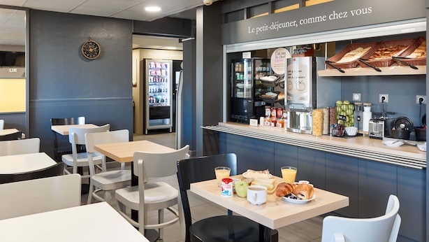 A café with tables and chairs, a refrigerator, and a display case with food items. - B&B HOTEL Corbeil-Essonnes (Corbeil-Essonnes)