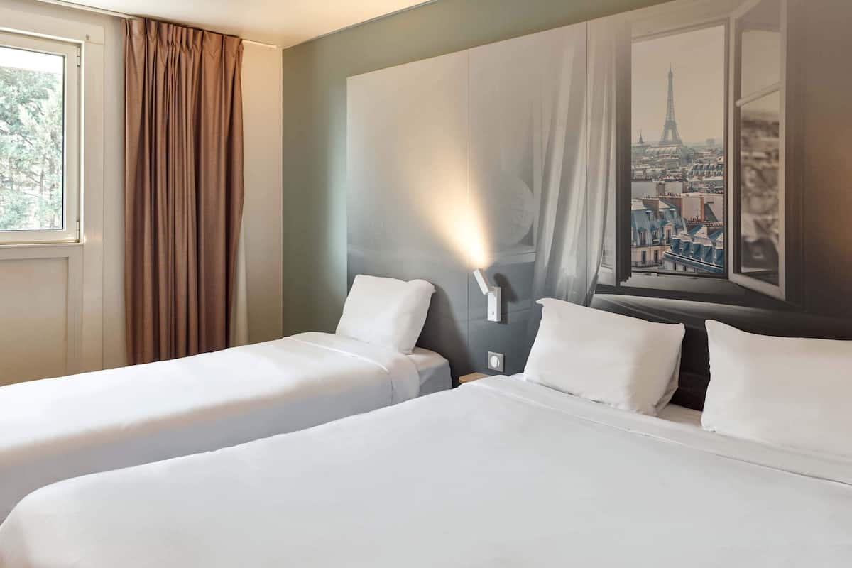 Habitación de hotel con dos camas individuales, un ventanal con vistas a la ciudad y una lámpara fijada a la pared.