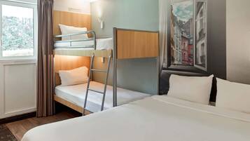 A hotel room with a bunk bed, a single bed, a ladder, a window with curtains, and a painting on the wall.