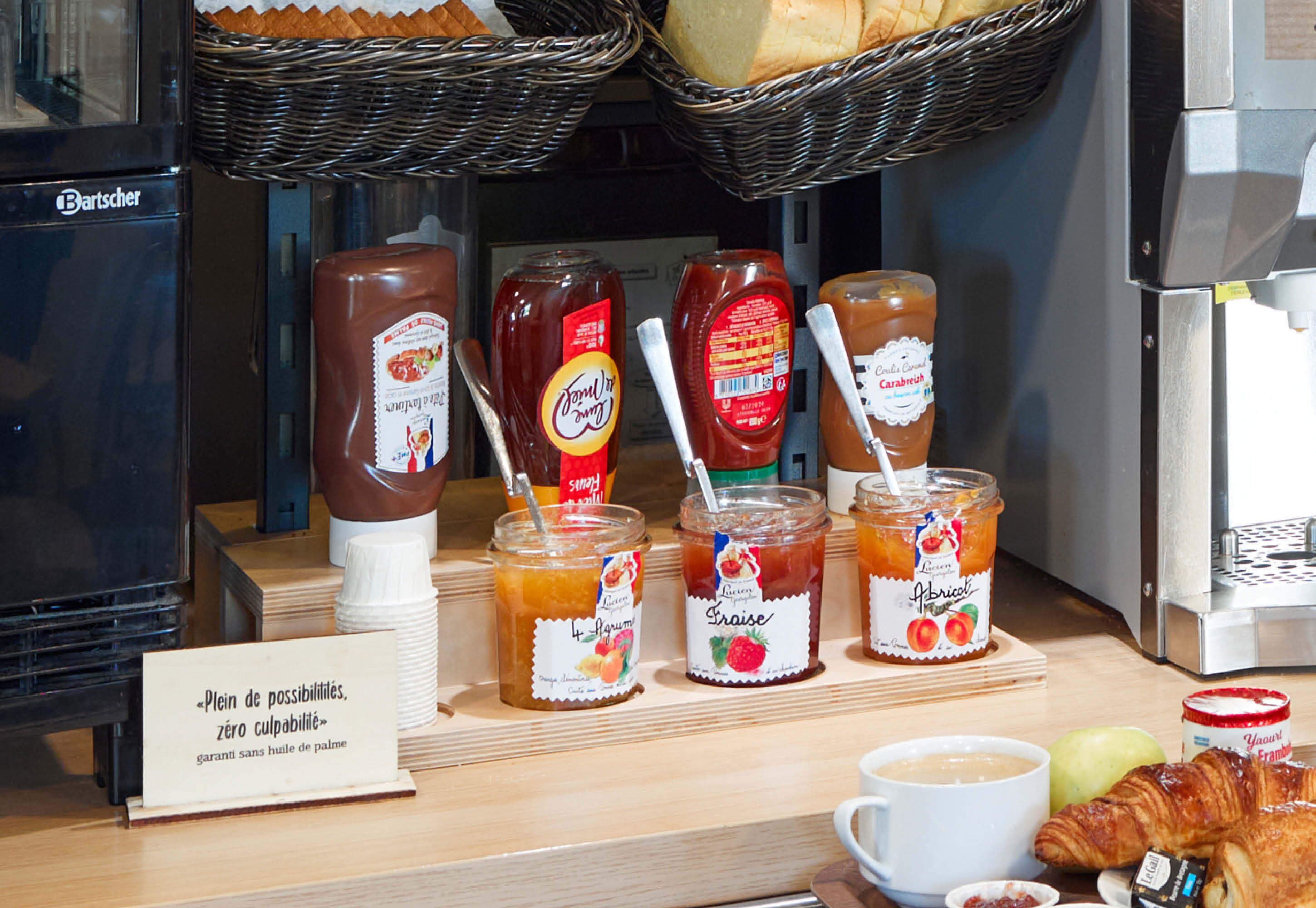 A breakfast display with various jams, a coffee cup, croissants, and a sign indicating no butter.