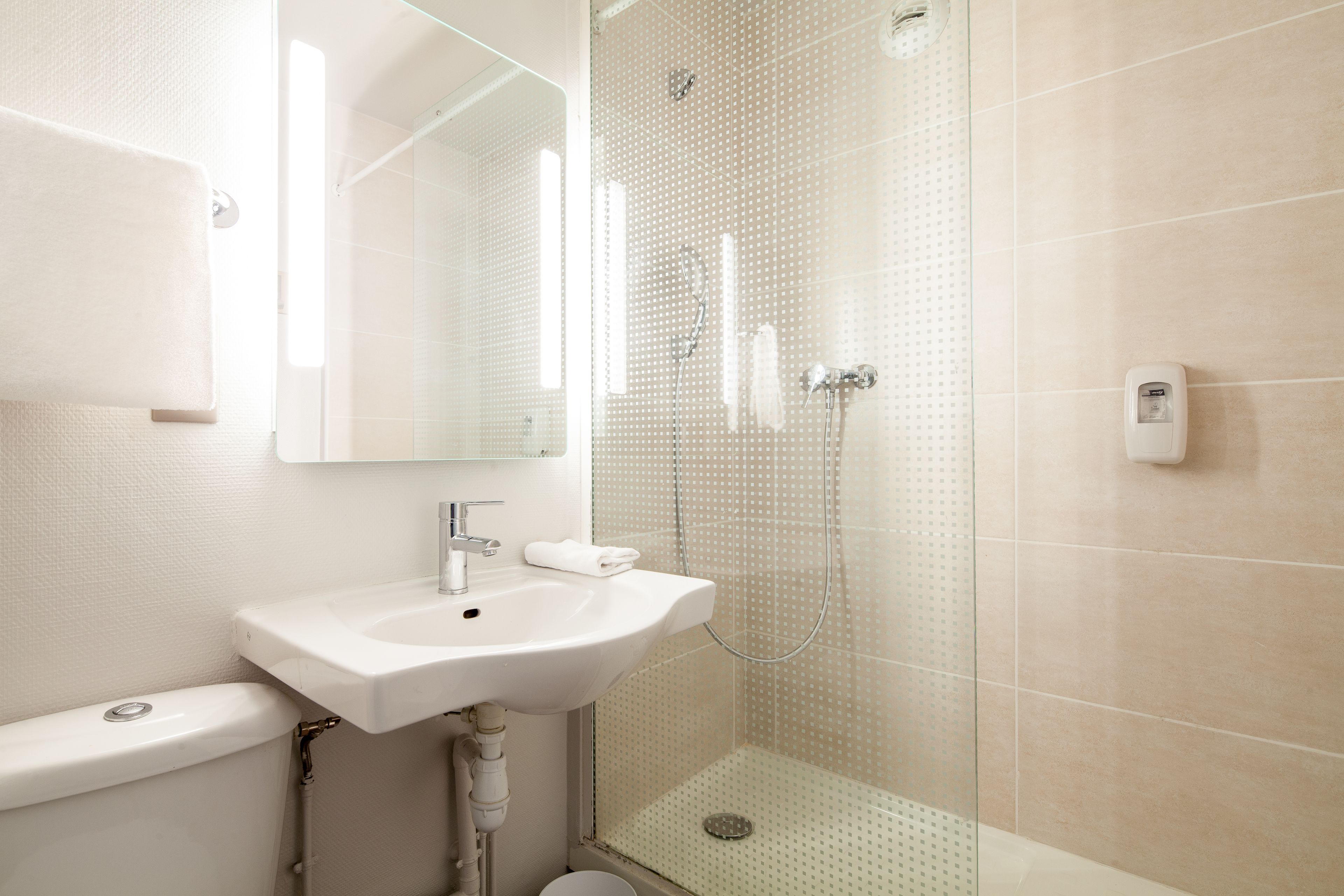 A modern bathroom with a white sink, mirror, and glass shower enclosure.
