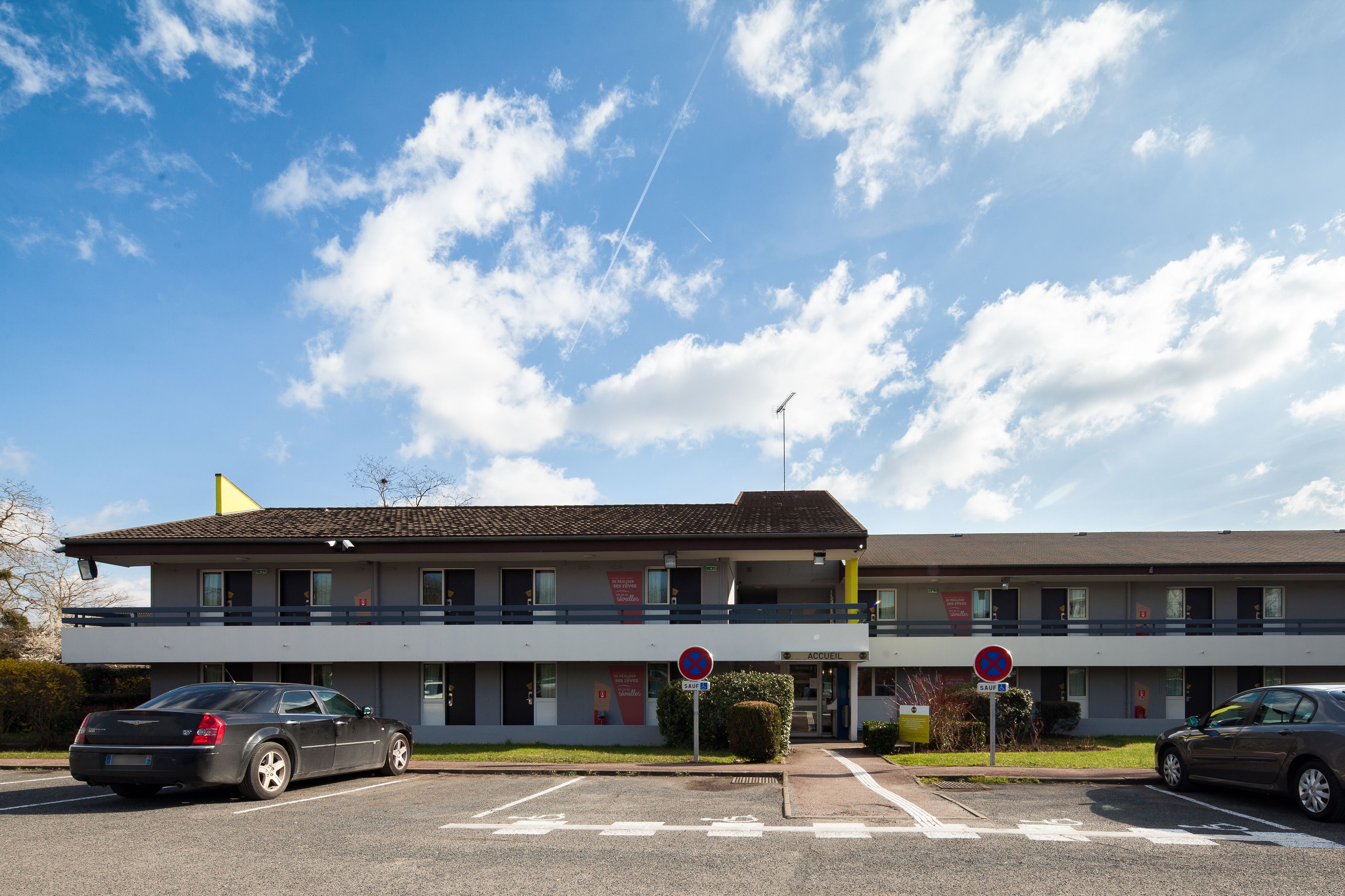 A two-story building with a parking lot, a no parking sign, and a clear sky.