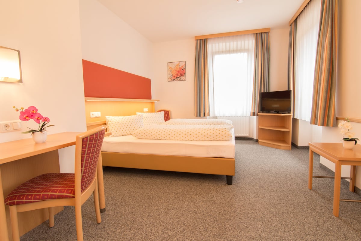 Habitación de hotel con cama, escritorio, silla, televisor y una mesita.