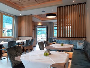 Un espace de repas moderne agrémenté de cloisons en bois, offrant différents types de sièges, notamment des tables et un canapé, ainsi que de grandes fenêtres donnant sur l’extérieur.