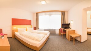 Una habitació d'hotel amb llit, escriptori, cadira, televisió i finestra amb cortines.