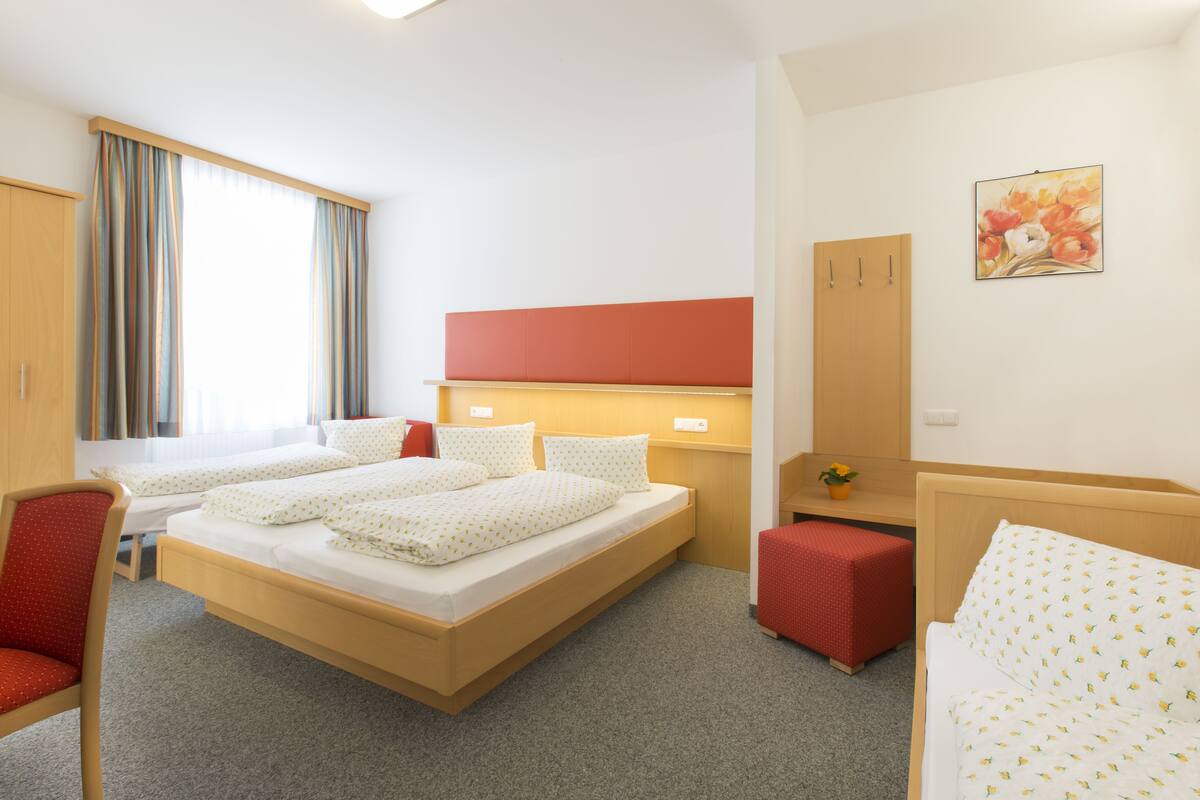 Habitación de hotel con dos camas, un escritorio, una silla, un armario y un cuadro en la pared.