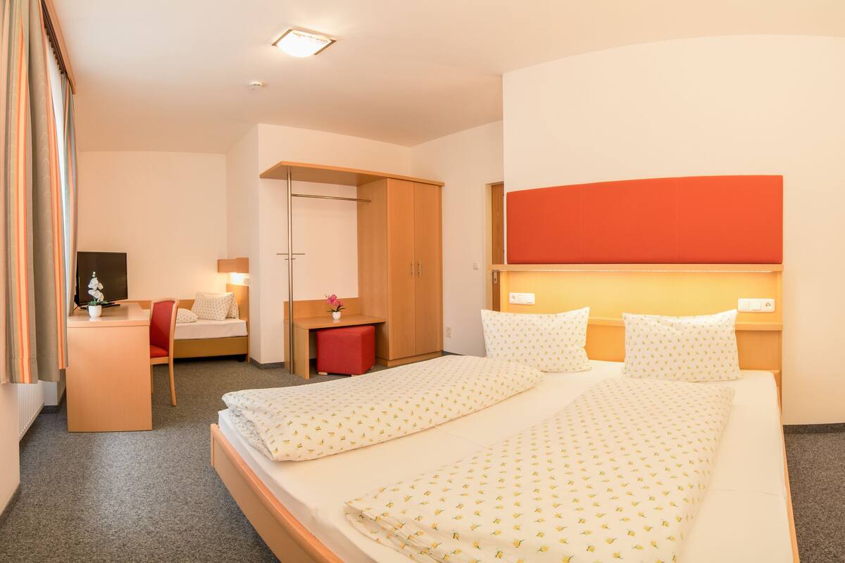 Una habitación de hotel con cama, escritorio, silla, televisión y espejo.