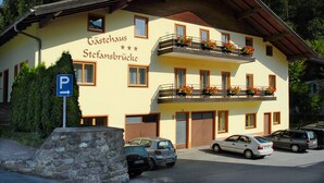 Edifici de dues plantes amb un rètol que diu "Gästehaus Stefansbrücke". Hi ha cotxes aparcats al davant i es pot veure un senyal blau d'aparcament.