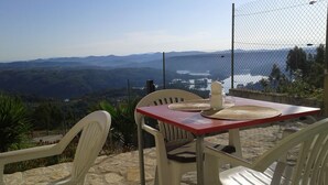 Mesa con dos sillas de plástico blanco, una vela y un mantel individual, con vistas a un paisaje montañoso.