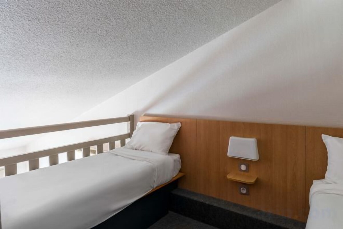Ein kleines Zimmer mit einem Einzelbett, einem Holzkopfteil, einem Nachttisch und einer Wandleuchte.