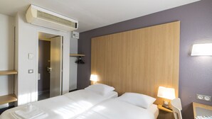 A hotel room with a bed, bedside tables, a lamp, an air conditioning unit, and a wooden headboard. - B&B HOTEL Auxerre Bourgogne (Moneteau)