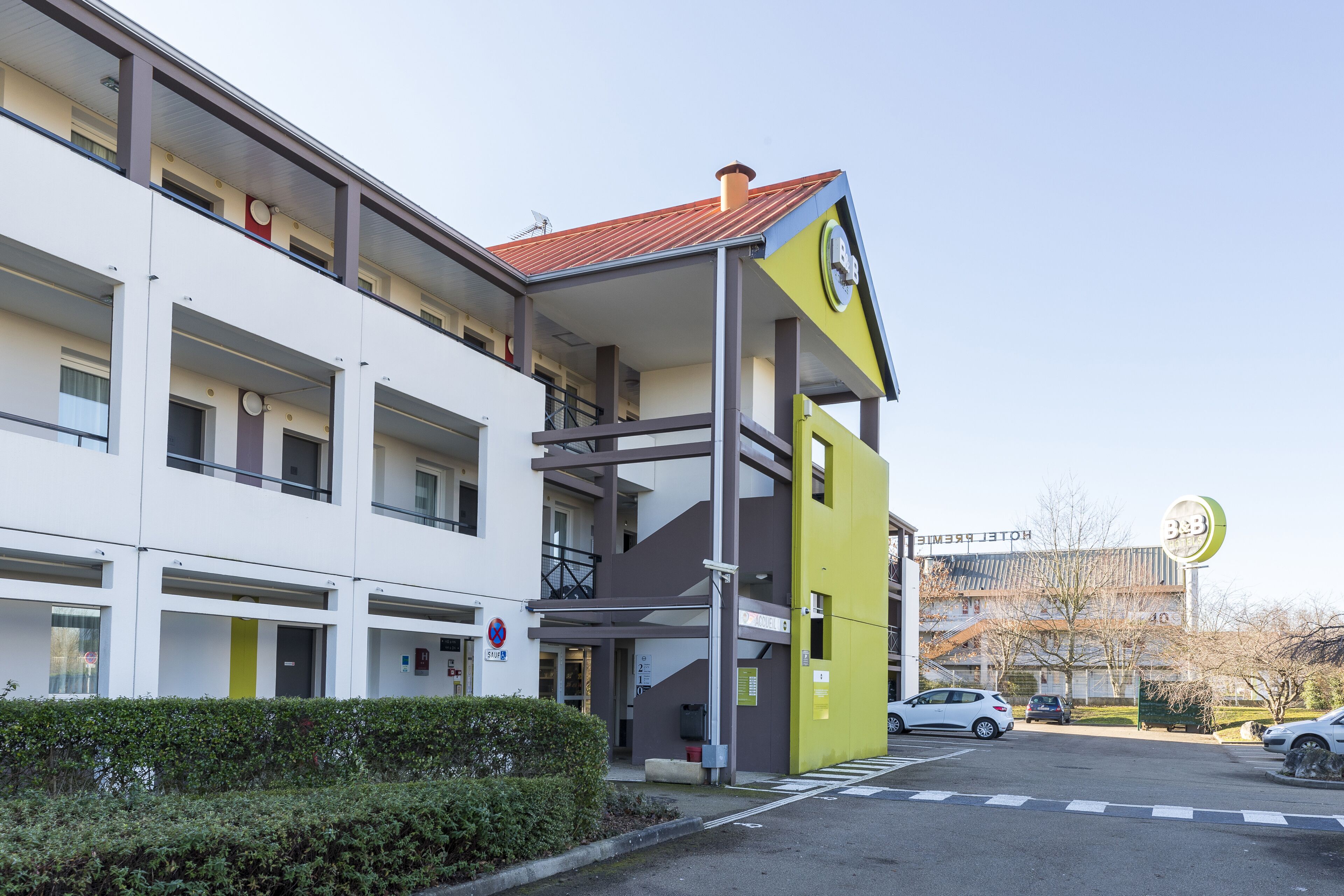 A modern hotel with a yellow and white facade, multiple balconies, and a parking area.