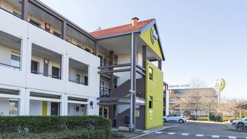 A modern hotel with a yellow and white facade, multiple balconies, and a parking area.