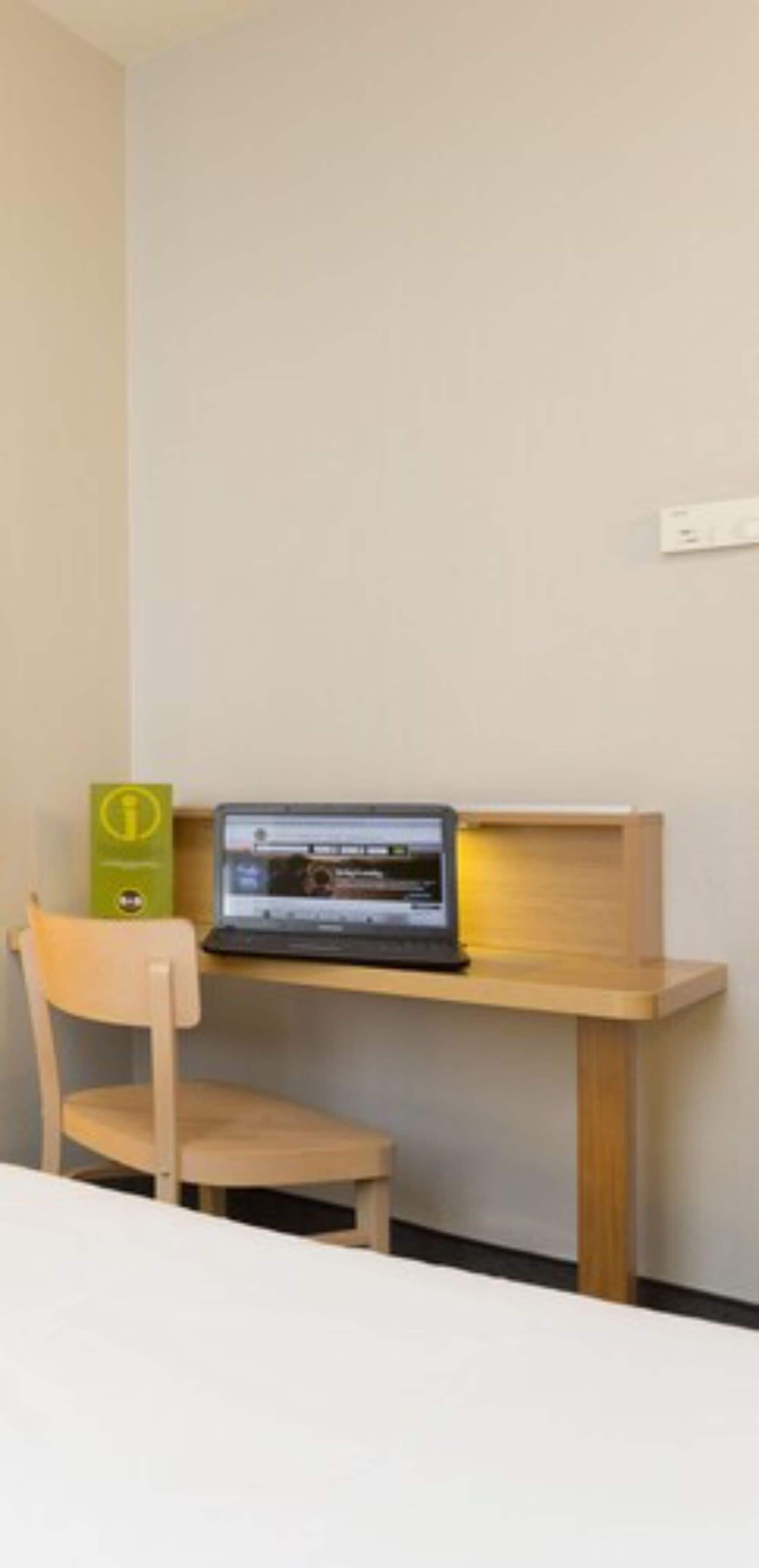 Un petit espace de travail avec un ordinateur portable posé sur un bureau en bois, une chaise et une boîte verte.