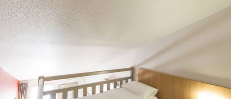 A single bed with a wooden headboard, a bedside table with a lamp, and a window with curtains.