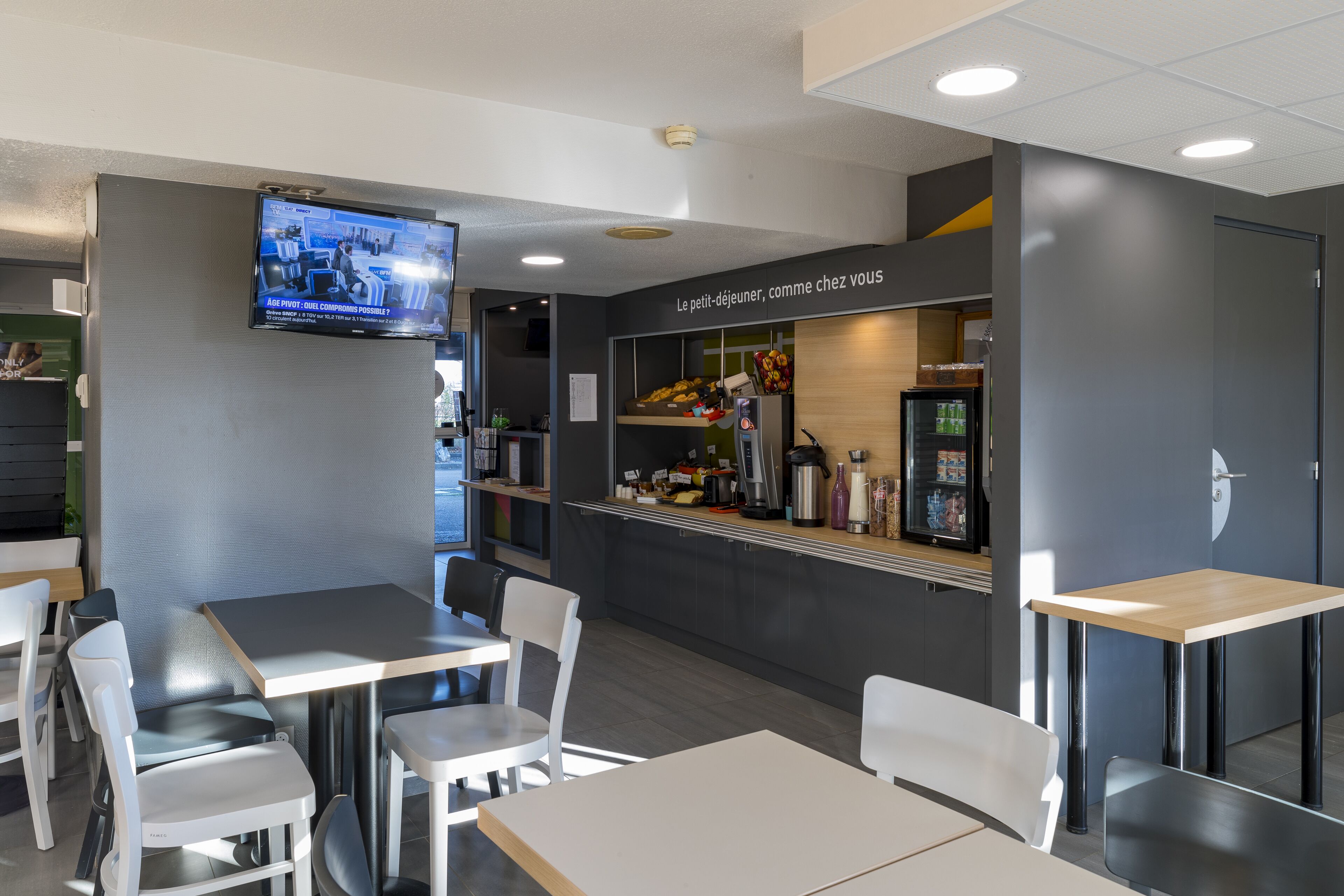 Un caffè moderno con tavoli e sedie, uno schermo televisivo e un bancone con diversi articoli.