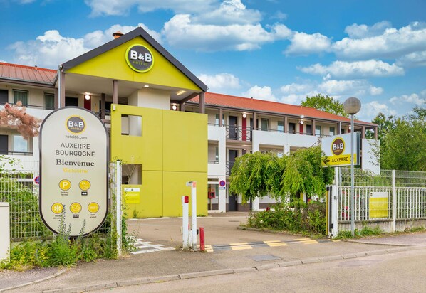 Un hôtel de type « bed and breakfast » avec une façade jaune, une enseigne indiquant les équipements disponibles, tels qu’un parking, une connexion Wi-Fi et un restaurant TGI.