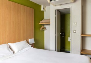 A hotel room with a bed, a wooden headboard, a green wall, a door, and a shelf with a hanger.