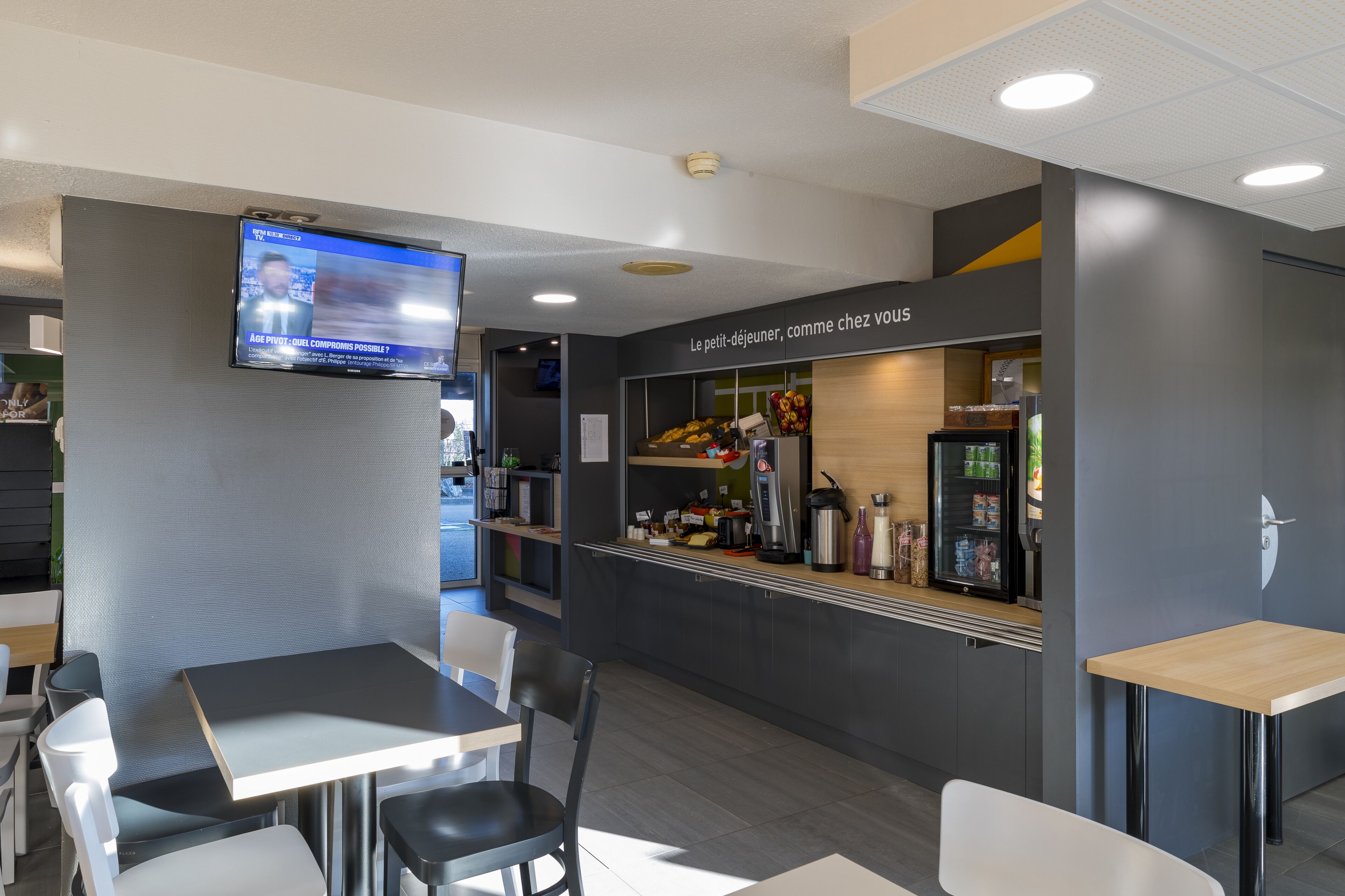 Ein modernes Café-Interieur mit Sitzgelegenheiten, einer Kaffeebar und einem Fernsehbildschirm, der eine Nachrichtensendung zeigt.