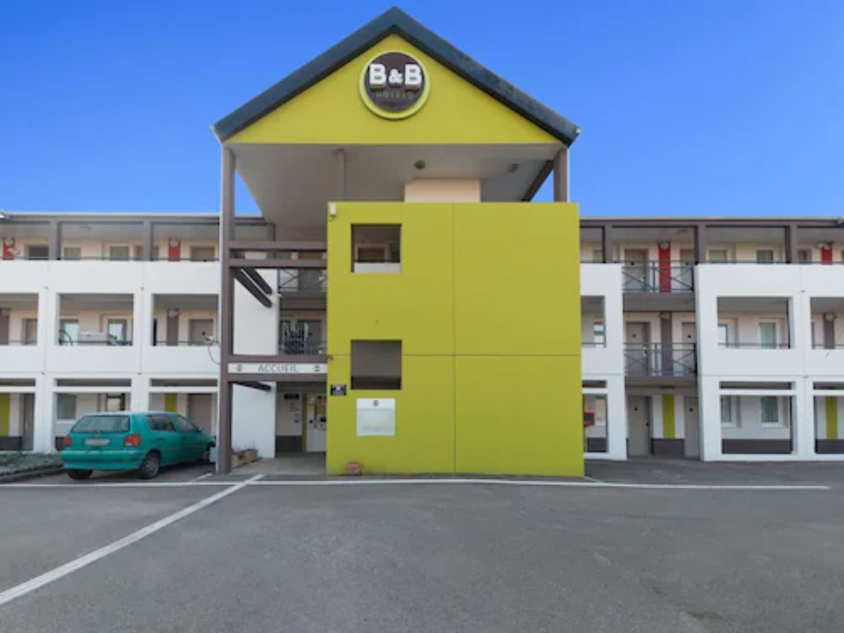Un hôtel à la façade distinctive, aux couleurs jaune et gris, avec une enseigne bien visible indiquant « chambre d’hôtes ».