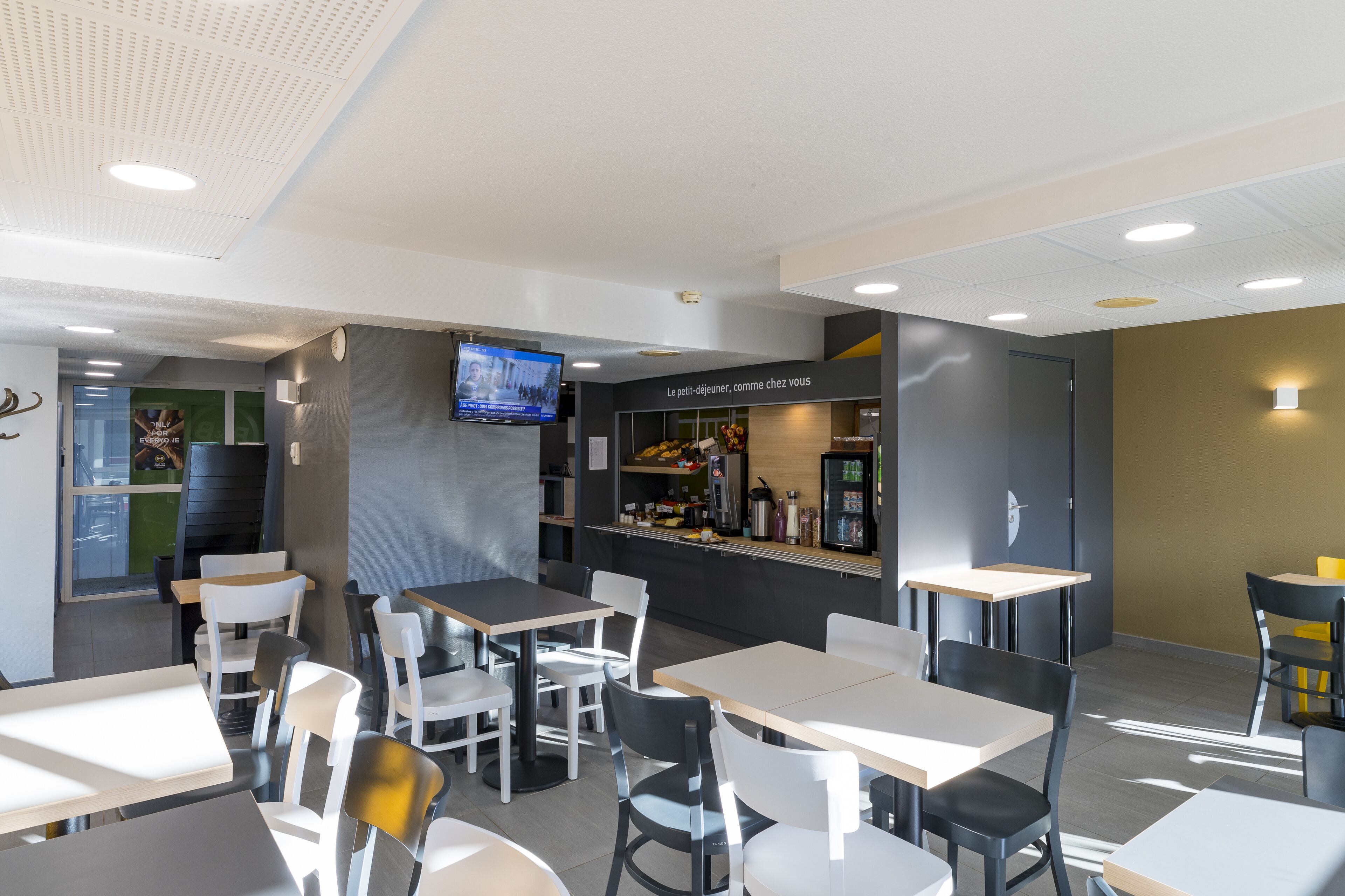 A modern cafe with tables and chairs, a TV screen, and a counter with a menu.