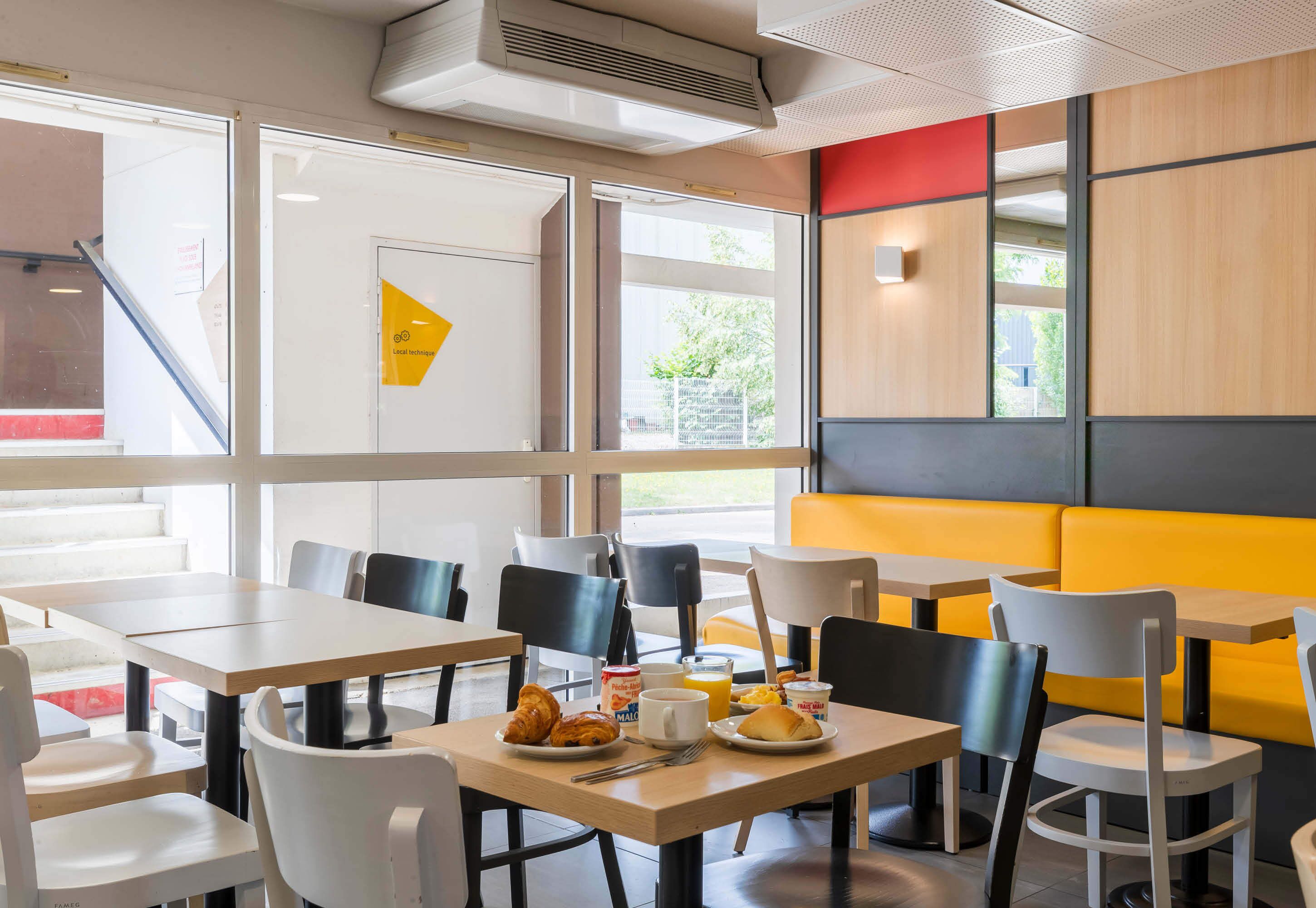 Un café moderno con mesas y sillas, un banco amarillo y vistas al exterior.