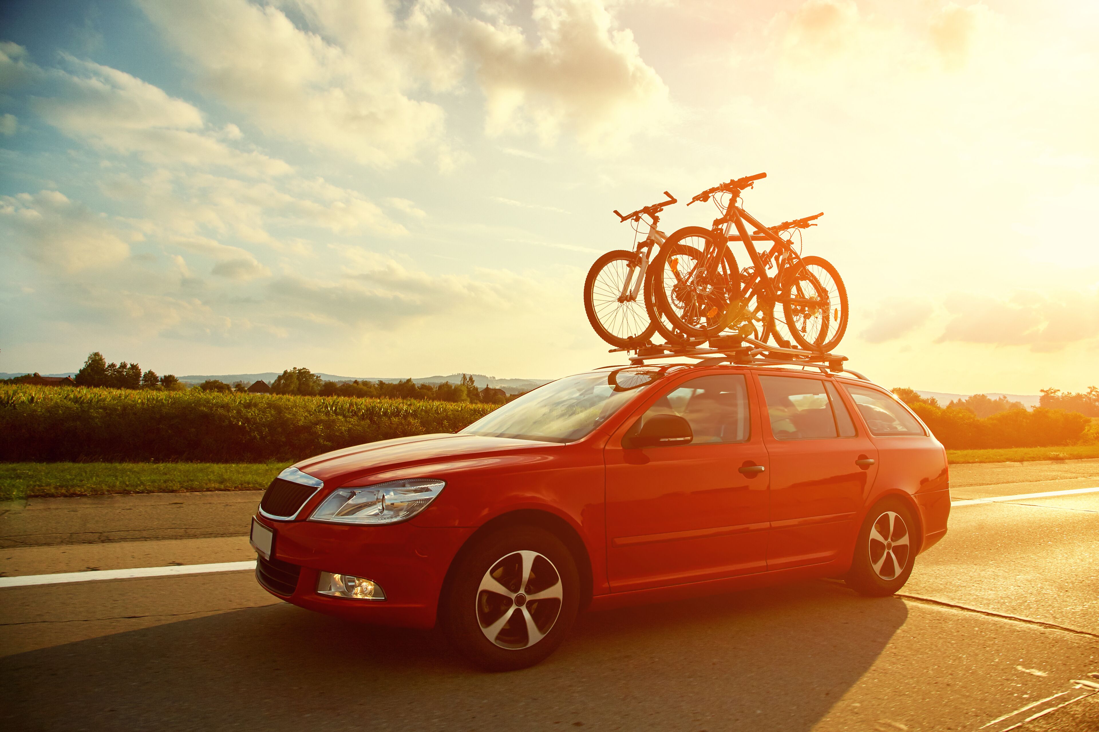 Une voiture rouge avec des vélos fixés sur le toit, garée sur une route par un temps clair.